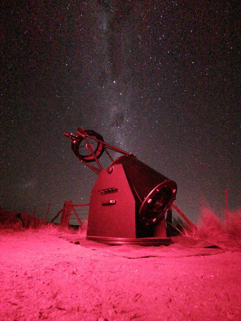 Telescopio dobsoniano iluminado con luz roja bajo un cielo estrellado